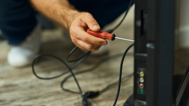 Handy home repair. Close up shot of hand of a repairman using a screwdriver while installing or fixing tv set indoors. Repair service concept.